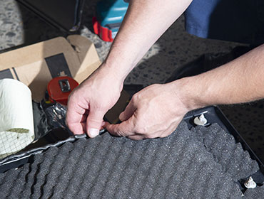 Fitting a dark acoustic foam layer into a vehicle floor pan.